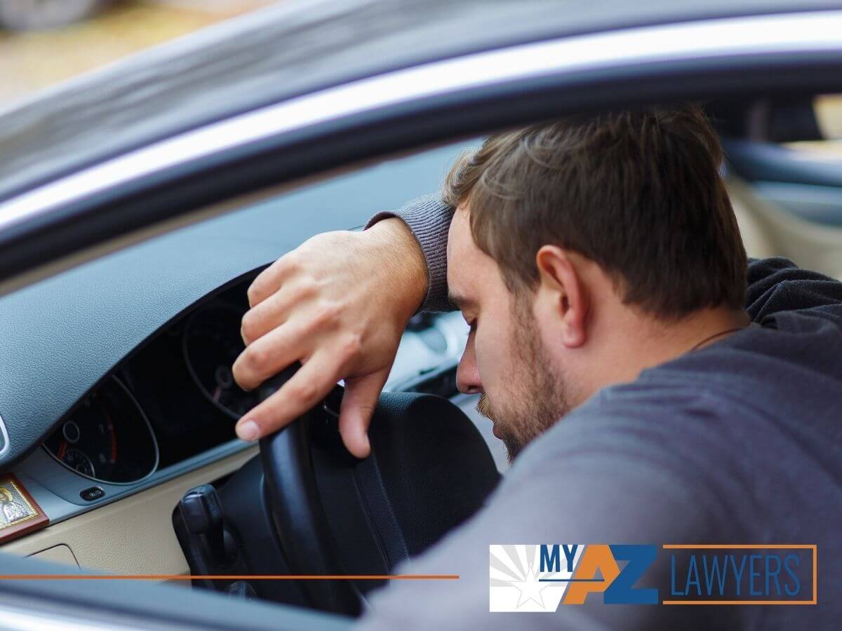 Arizona DUI Lawyer, Man lying on a steering wheel lying on a steering wheel, unable to drive a car.