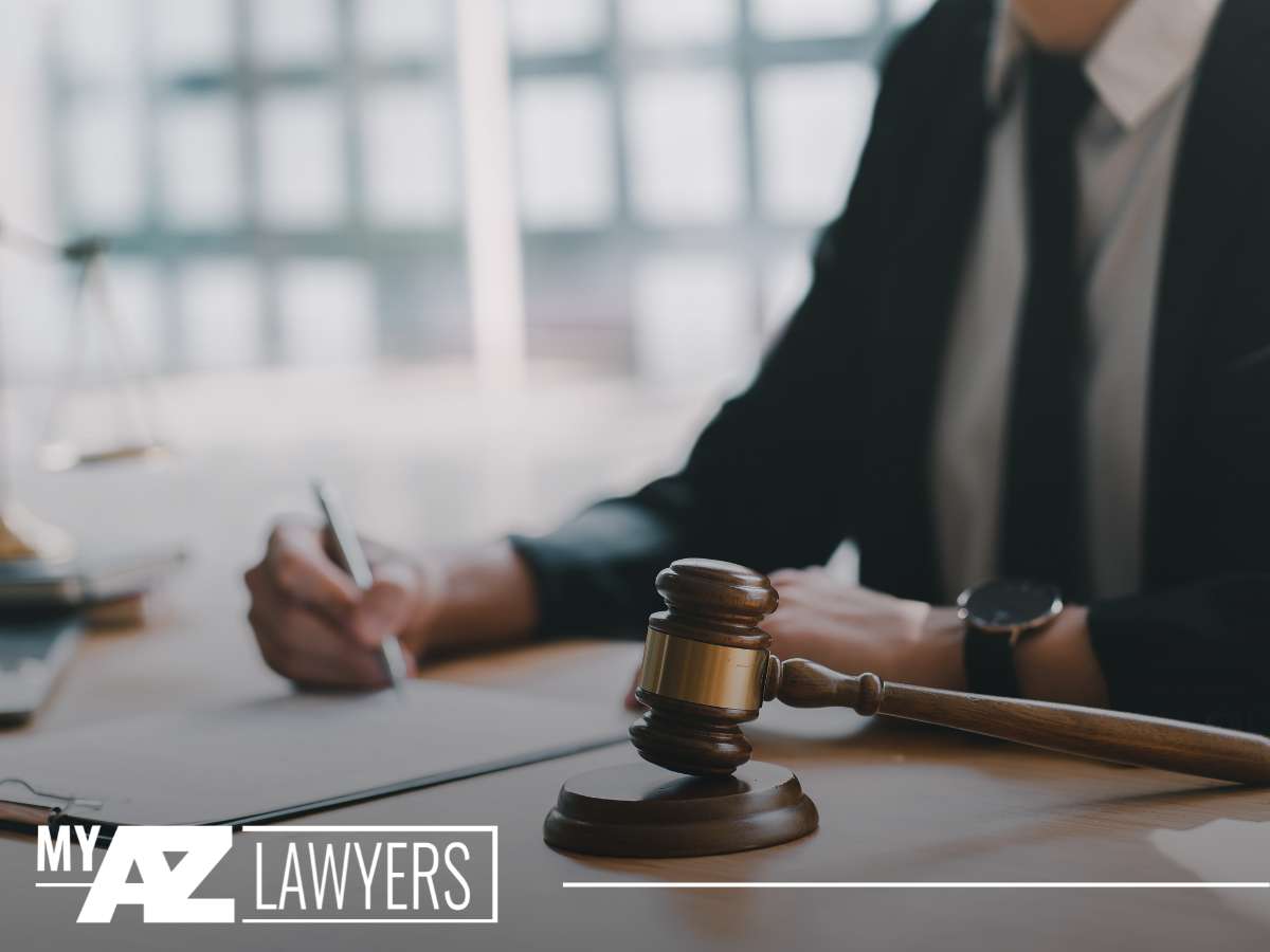 A close-up image of a person in a business suit sitting behind a desk, pen in hand, with a wooden gavel in the foreground, symbolizing legal proceedings